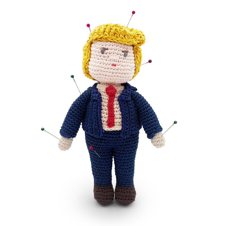 Crochet Trump voodoo doll with colorful pins, yellow hair, a navy suit and a red tie, shown from the front.
