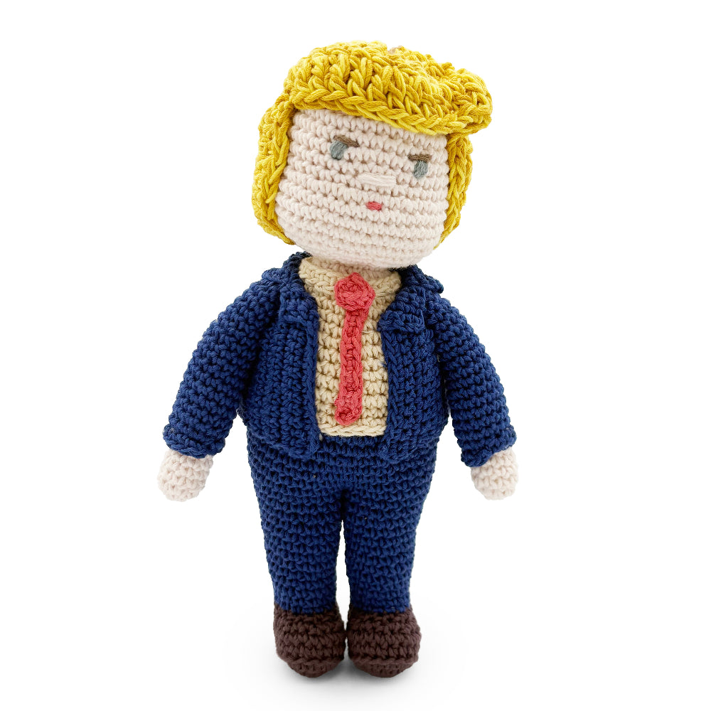 Front view of a handmade crochet Trump doll with yellow hair, a navy suit, red tie and brown shoes.