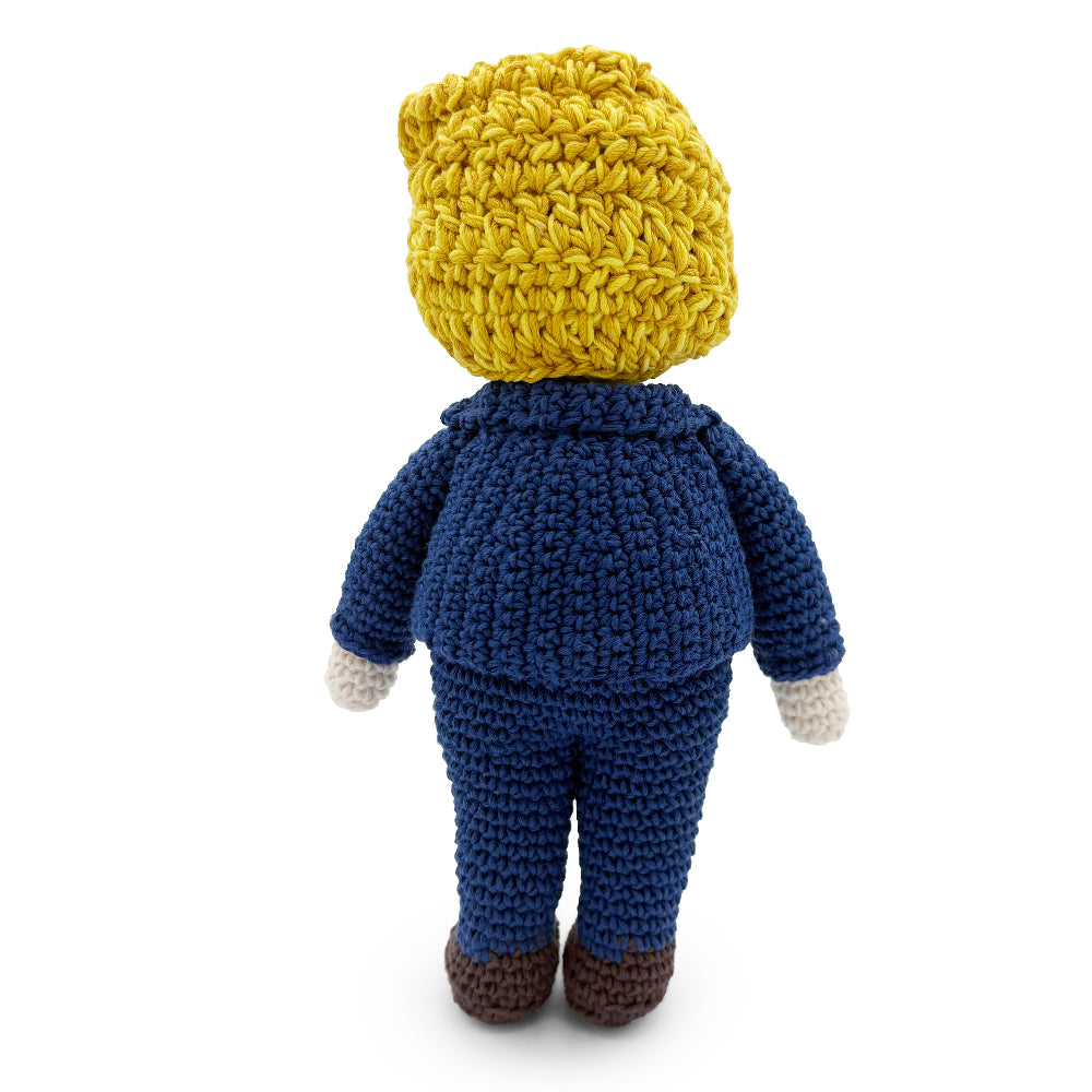 Back view of a crochet Trump doll showing textured yellow yarn hair and a navy suit.